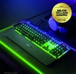 RGB backlit mechanical gaming keyboard on a desk with a blue headset nearby; yellow award sticker reading 'APEX 7 Mejor Teclado Gaming'