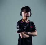 Esports player with arms crossed, wearing a black team jersey and a large over-ear headset against a gray background.
