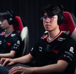 Two esports players wearing headphones sit at gaming desks, focused on the screen in a dim studio.