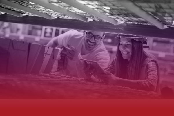 Two coworkers in a factory inspect parts on a conveyor, smiling as they work together.