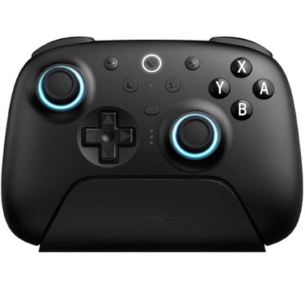 Black wireless game controller with blue-lit thumbstick rings resting on a charging dock.