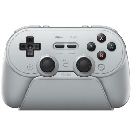 Silver 8BitDo Pro 3 wireless game controller resting in a charging dock, with D‑pad, two thumbsticks, and X/Y/A/B buttons.