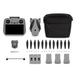 Quadcopter drone with controller and accessories: spare propellers, bag, tools, batteries, and charger laid out on a white surface.