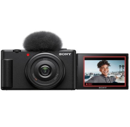 Sony action camera with a flip-out LCD screen showing a smiling person in a sunny outdoor setting; black body with attached mic on top.
