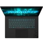 Top-down view of a black laptop open with teal backlit keyboard; screen displays a blue Gigabyte logo.