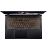 Top-down view of a black laptop with orange backlit keyboard and trackpad visible on a dark surface.”,