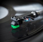 Close-up of a turntable tonearm with a green stylus tracing a vinyl record.